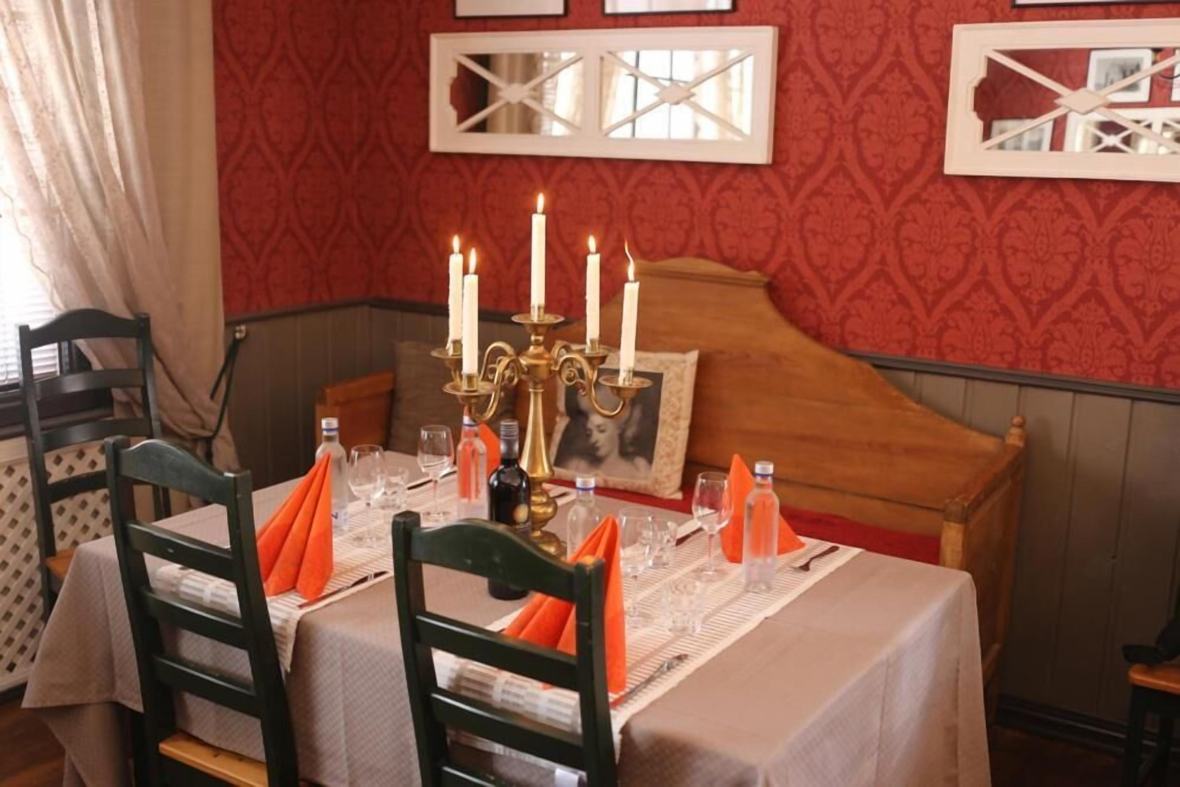 Una mesa de comedor dispuesta con velas, copas y servilletas, con un cabecero de madera y papel tapiz estampado en el fondo.