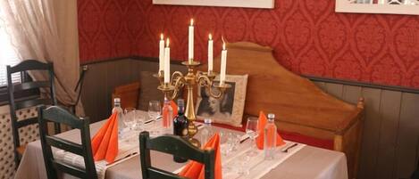Una mesa de comedor dispuesta con velas, copas y servilletas, con un cabecero de madera y papel tapiz estampado en el fondo.