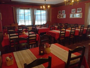 Un restaurant avec de nombreuses tables recouvertes de nappes rouges, des chaises en bois et un lustre.