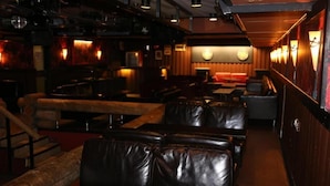 A dimly lit restaurant interior with leather booths, wooden tables, and a bar area. - Hotel Kievari Ylitornio (Ylitornio)