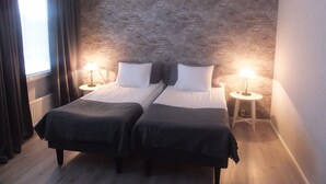 A room with two beds, a brick wall, a window with curtains, and two bedside tables with lamps. - Hotel Kievari Ylitornio (Ylitornio)