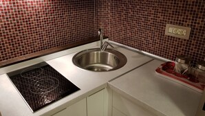 Uma cozinha com pia de aço inoxidável, um fogão por indução Bosch e uma tábua de corte vermelha e branca com utensílios.