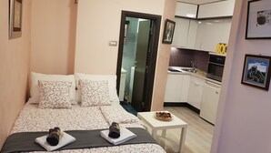 Quarto compacto com uma cama, uma mesinha com um prato de comida e uma cozinha compacta com armários e pia.
