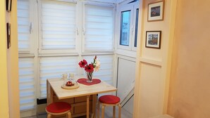 Uma pequena sala de jantar com uma mesa, duas cadeiras, um vaso com flores e duas chávenas.