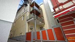 A multi-story building with a balcony on the second floor, a red awning on the right, and a closed metal gate at the entrance. - Apartments Kreuzgasse (Zell am See)
