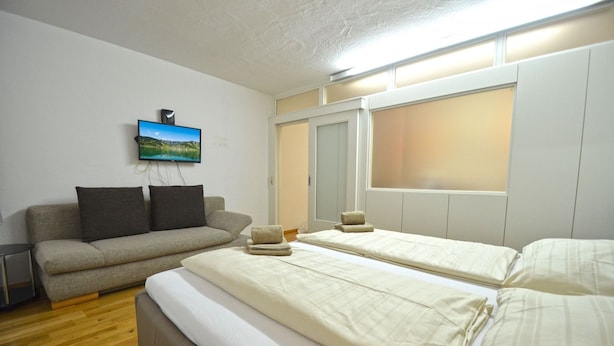 A hotel room with a sofa, two beds, a TV, and a window. - Apartments Kreuzgasse (Zell am See)