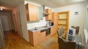A compact kitchen with wooden cabinets, a built-in microwave, a stove, and a coffee maker. - Apartments Kreuzgasse (Zell am See)