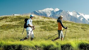 Two hikers walking on a grassy hill with a mountain range in the background. - Apartments Kreuzgasse (Zell am See)