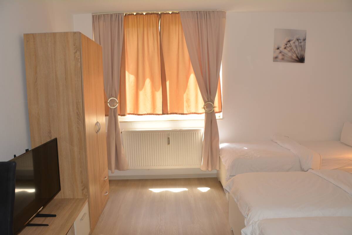Une chambre à coucher avec un lit, une télévision et une fenêtre avec des rideaux.