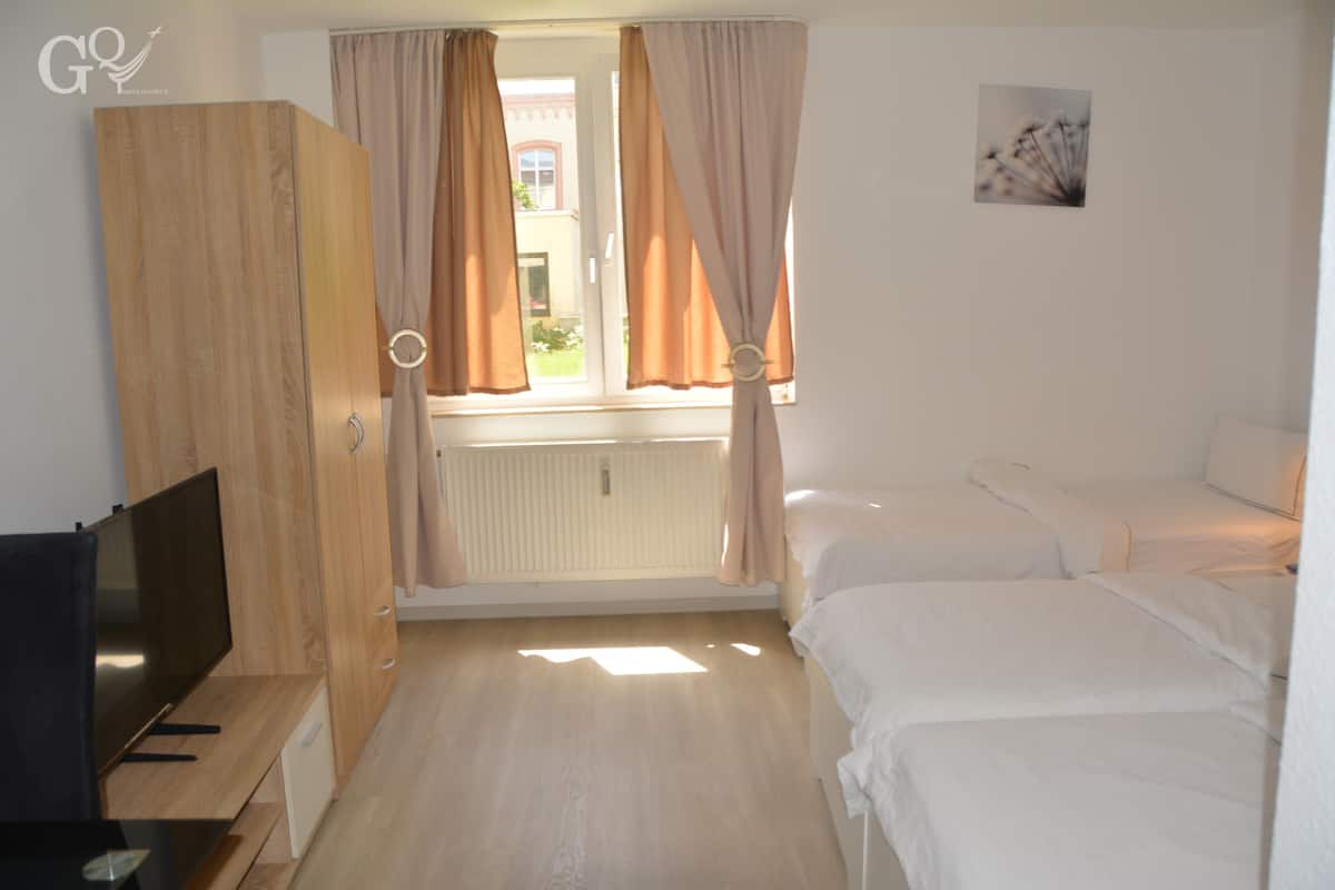 Une chambre avec une télévision, une armoire en bois, deux lits et une fenêtre avec des rideaux.