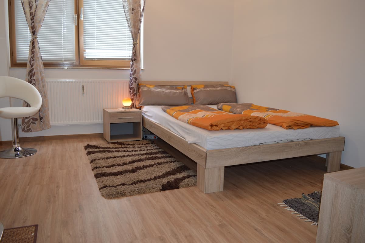 Une chambre à coucher comprenant un lit, une table de chevet, une lampe, une chaise et une fenêtre avec des rideaux.