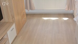 A room with a wooden floor, a white cabinet with drawers, a radiator, and a window with curtains. - Saarbrücken City Apartments (Saarbrücken)