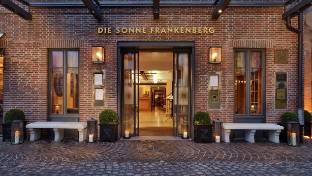 The entrance of Die Sonne Frankenberg hotel with a brick facade, glass doors, and a cobblestone pathway leading to a bench. - Die Sonne Frankenberg (Frankenberg)
