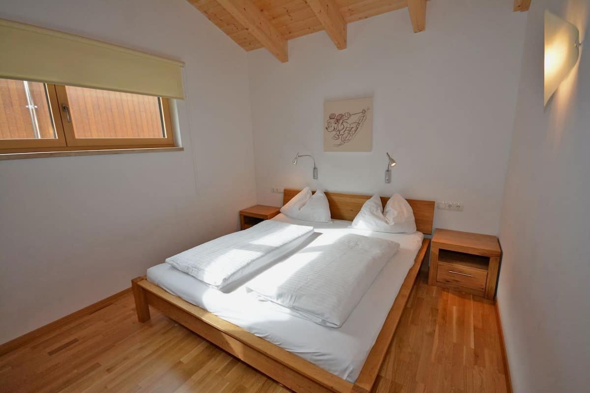 Une chambre à coucher avec un lit en bois, deux tables de chevet, une fenêtre avec des stores et une lampe fixée au mur.