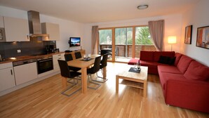 A modern kitchen with a dining area, a red sofa, and a large window with a view of trees. - Schmitten Finest Apartments (Zell am See)
