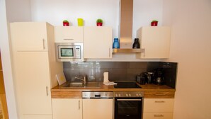 A compact kitchen with a microwave, stove, oven, and sink. There are cabinets and a countertop with a few items on it. - Schmitten Finest Apartments (Zell am See)