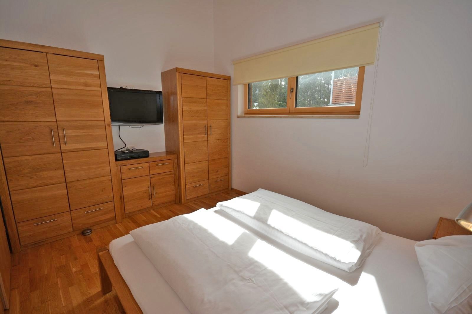 A bedroom with a bed, wooden wardrobe, and a television on a stand.