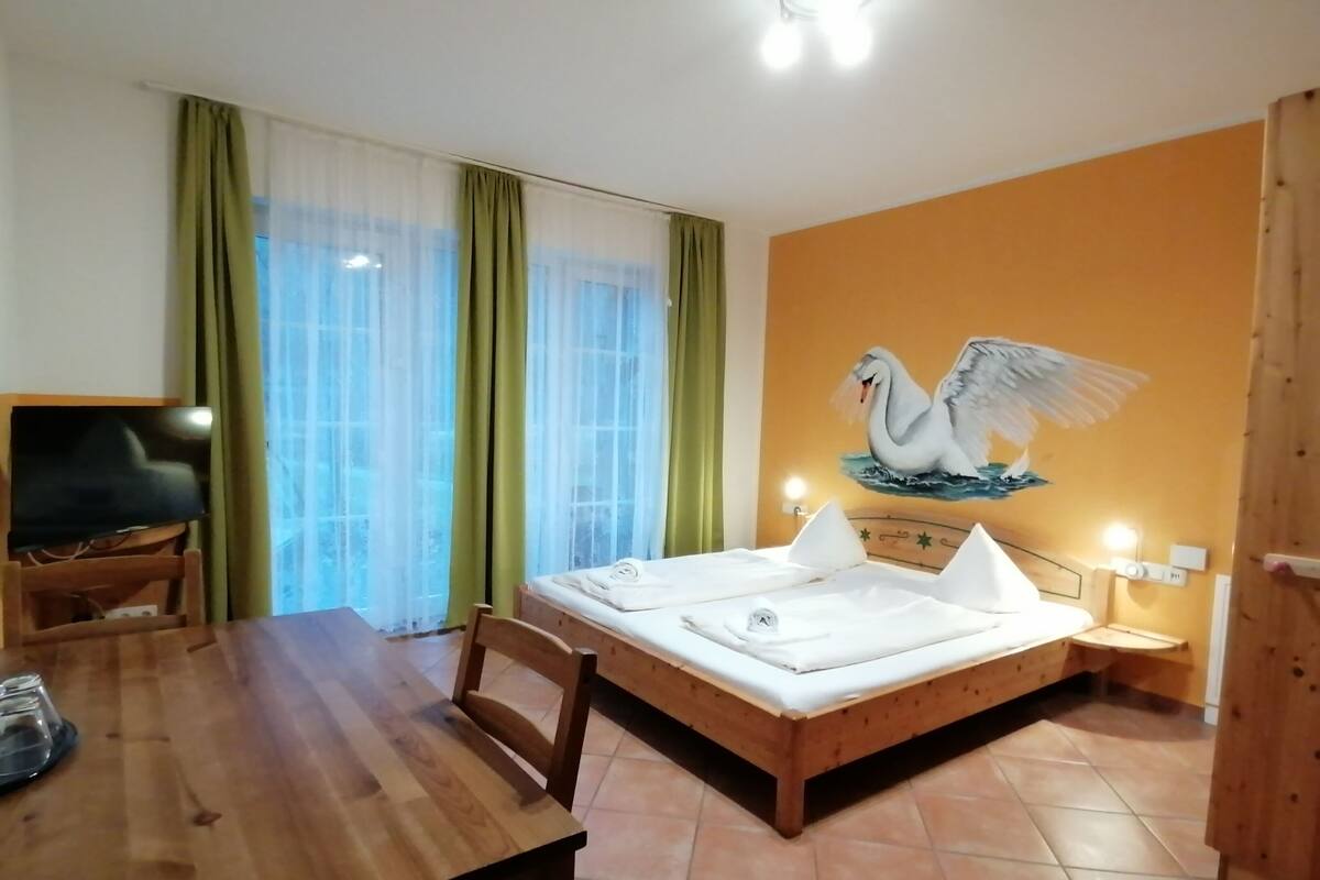A room with a wooden bed, a dining table, and a TV.