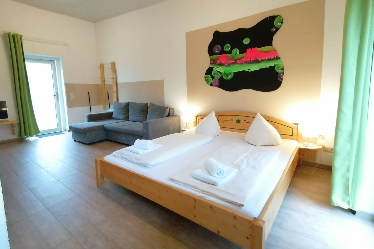 A bedroom with a wooden bed, a grey sofa, a green curtain, and a wall art piece.