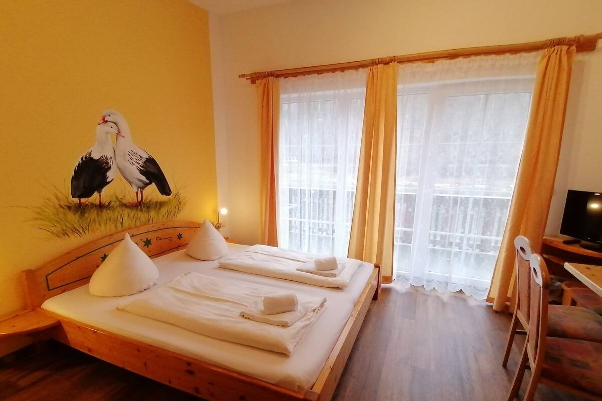 A hotel room with a wooden bed, two pillows, a flat-screen TV, and a painting of birds on the wall.