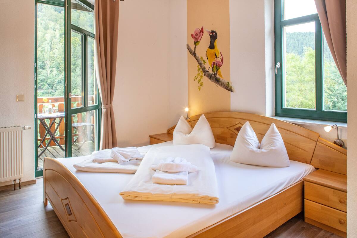 A neatly made bed with pillows and towels, a wooden headboard, and a painting of a bird on the wall.