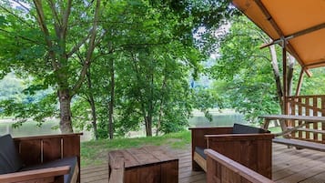 An outdoor wooden deck with seating, surrounded by trees and overlooking a body of water.