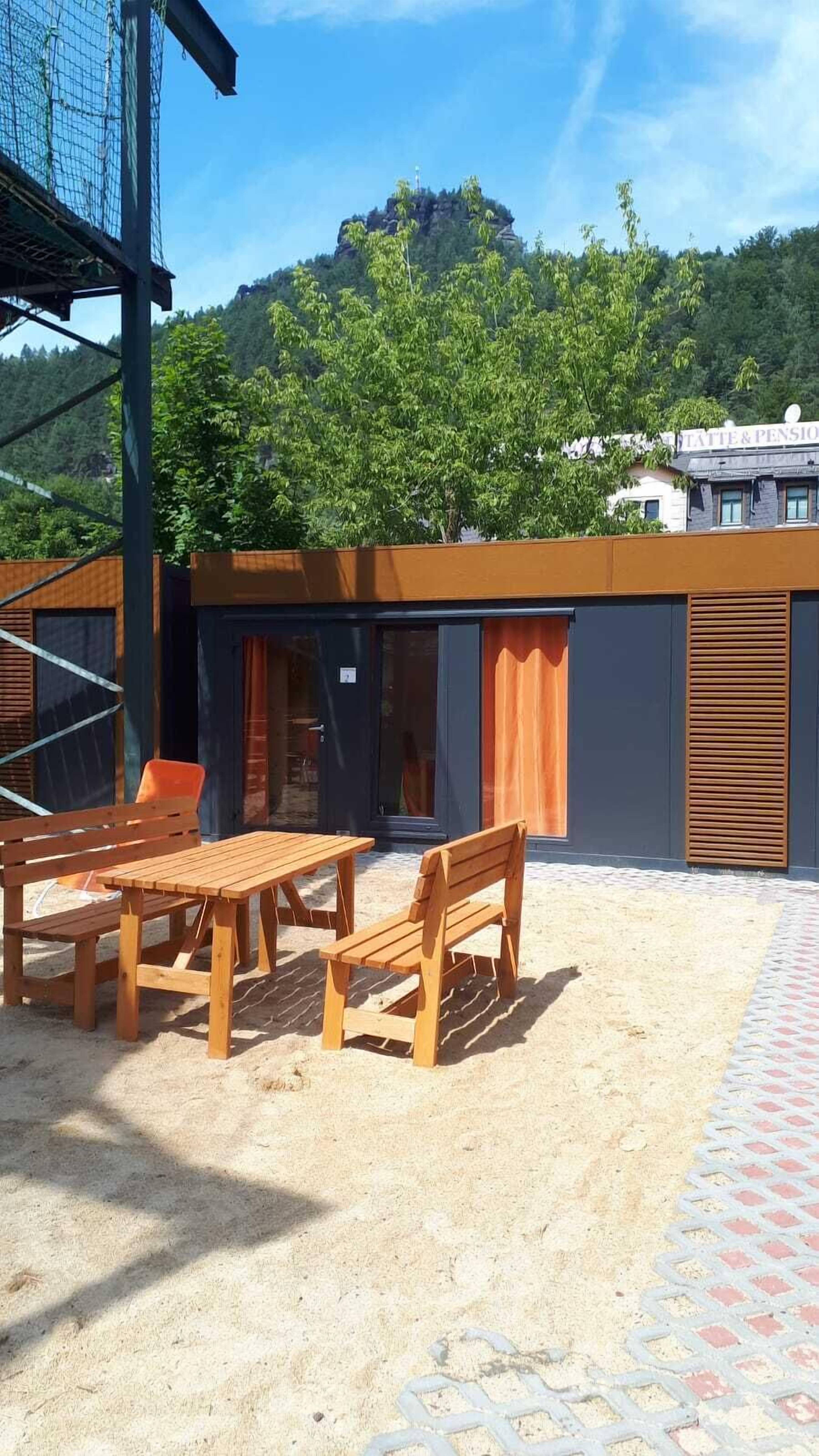 Et moderne udendørs opholdsområde med træmøbler, en overdækket terrasse og udsigt til et bjerg og træer.