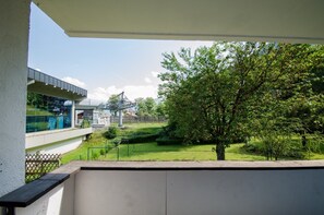 A balcony with a view of a modern building, a tree, and a well-maintained lawn.