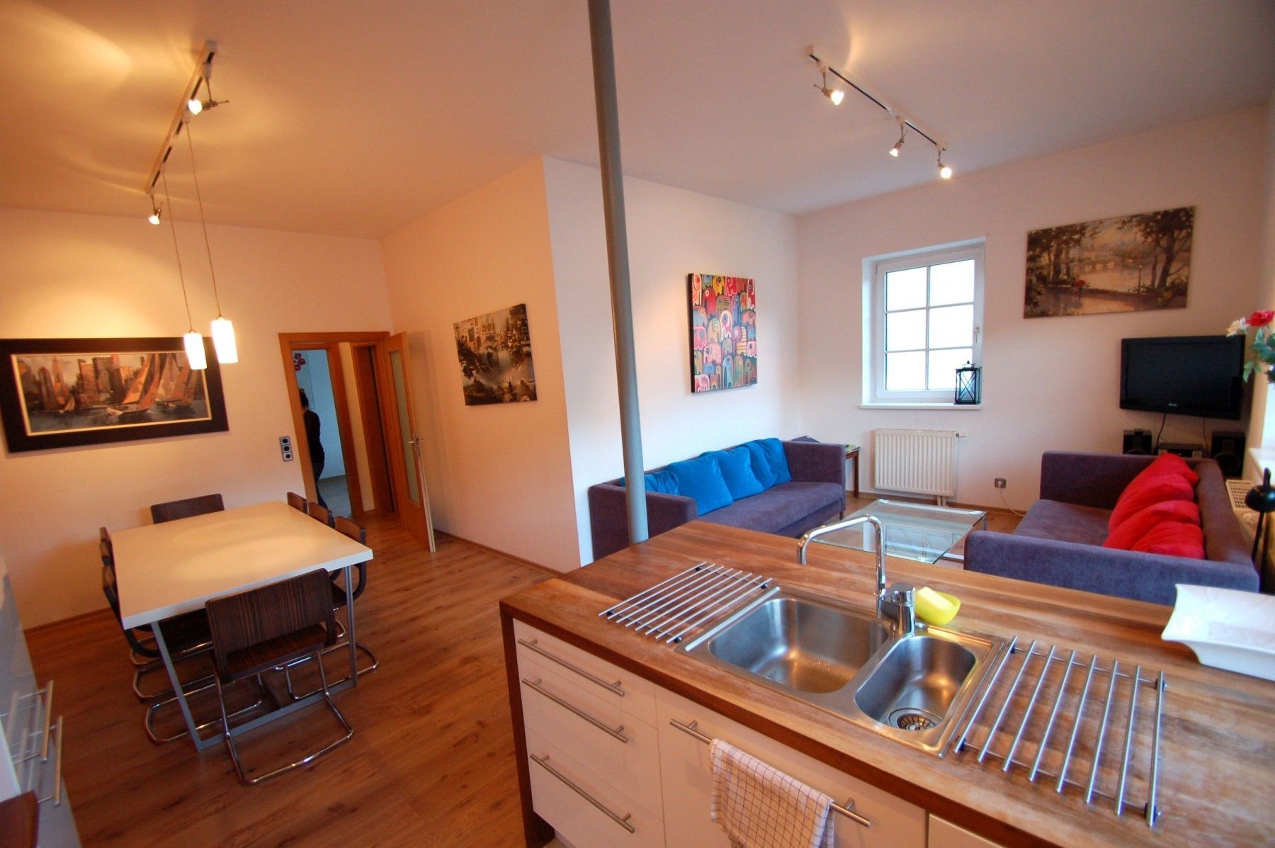 A modern living room with a sofa, a dining table, and a kitchen area with a sink and a window.