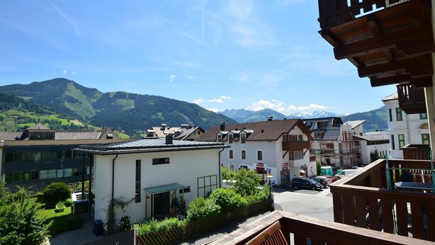 A residential area with modern and traditional buildings, a clear sky, and mountains in the background. - Apartments CityXpress (Zell am See)