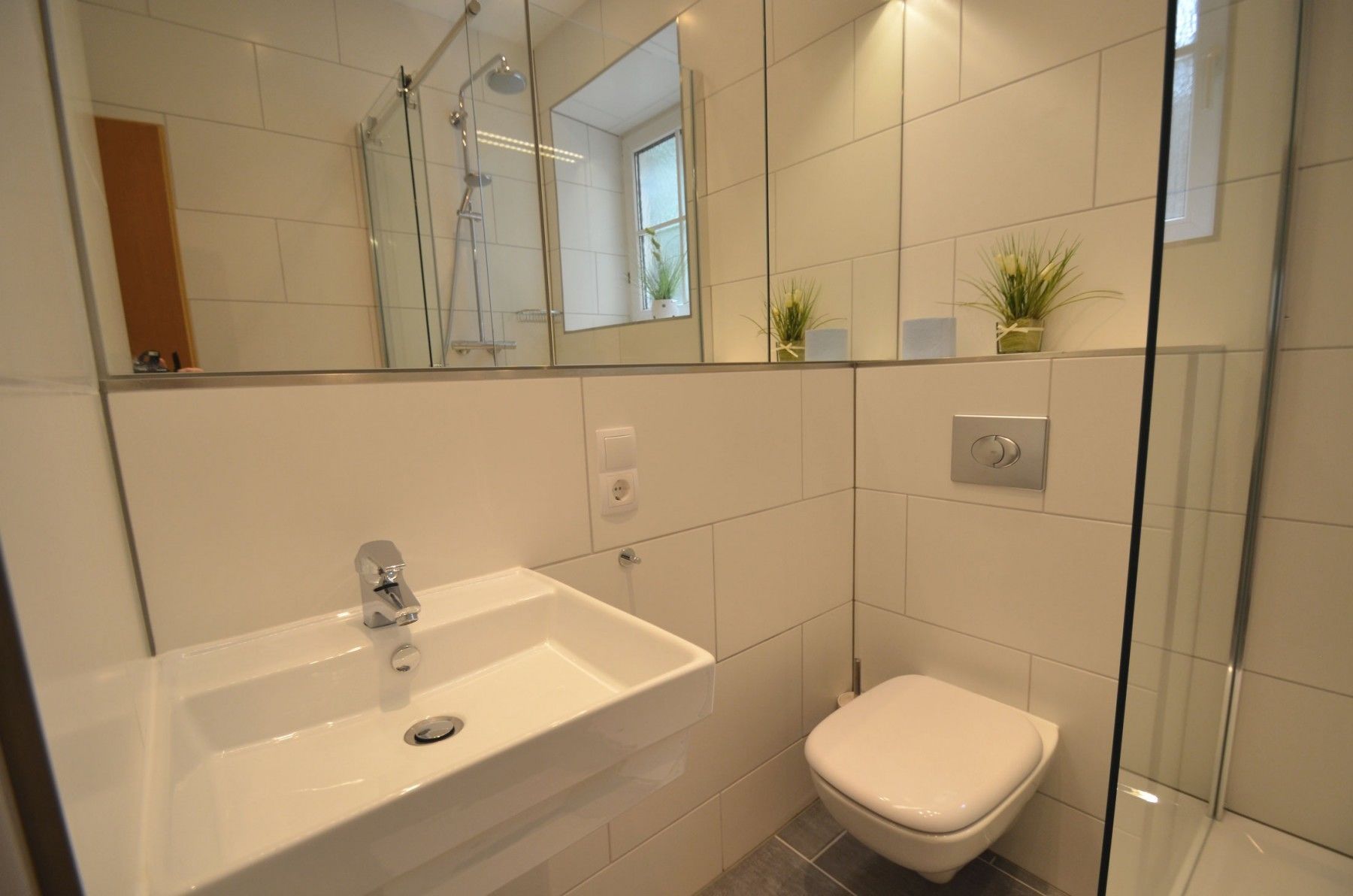 A modern bathroom with a white sink, a toilet, and a glass shower enclosure.