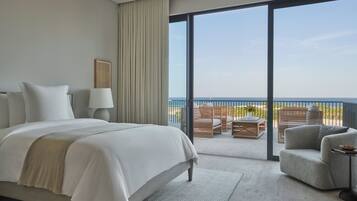 A hotel room with a large bed, a sitting area with a view of the sea, and a balcony with outdoor furniture.