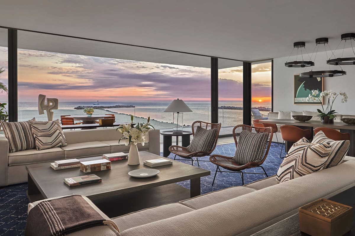 A modern living room with a large window overlooking a sunset view, furnished with a sofa, chairs, and a coffee table.