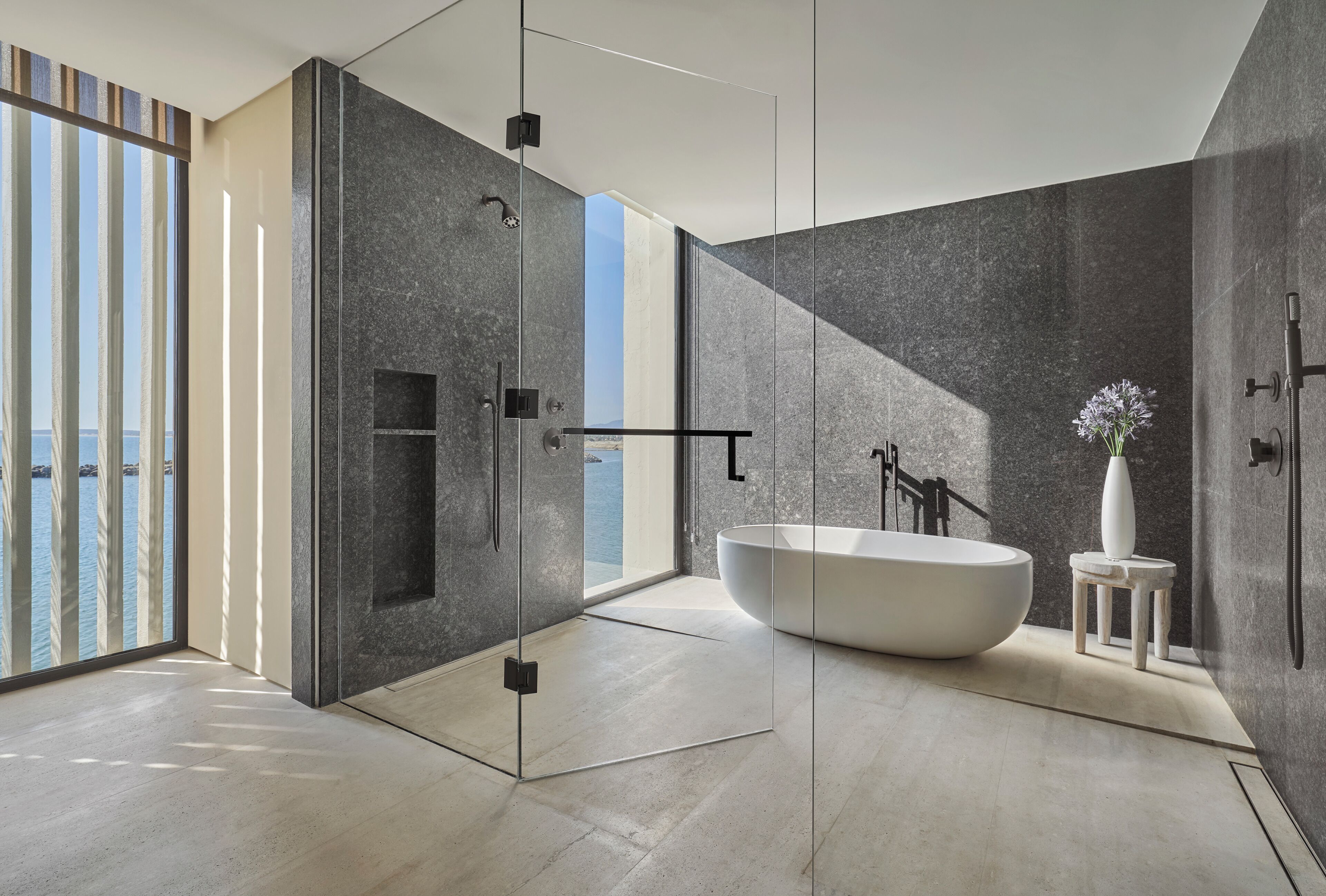 Un baño moderno con una bañera independiente, cabina de ducha de vidrio y vistas al mar.