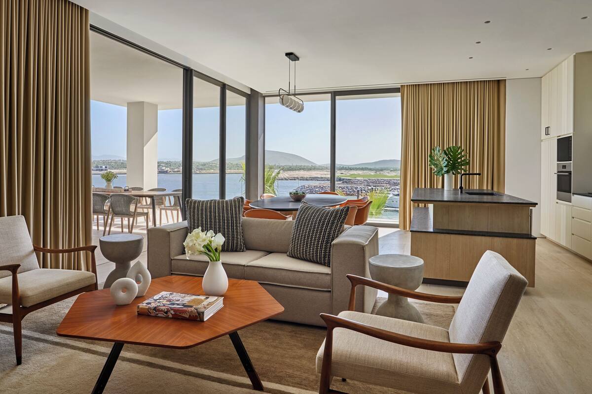 A modern living room with a sofa, chairs, a coffee table, and a view of the sea.