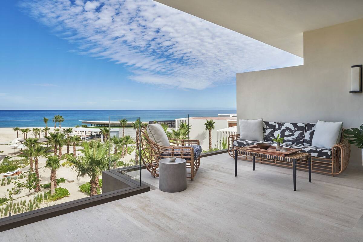 A balcony with wicker furniture, a view of the beach, and a clear sky.