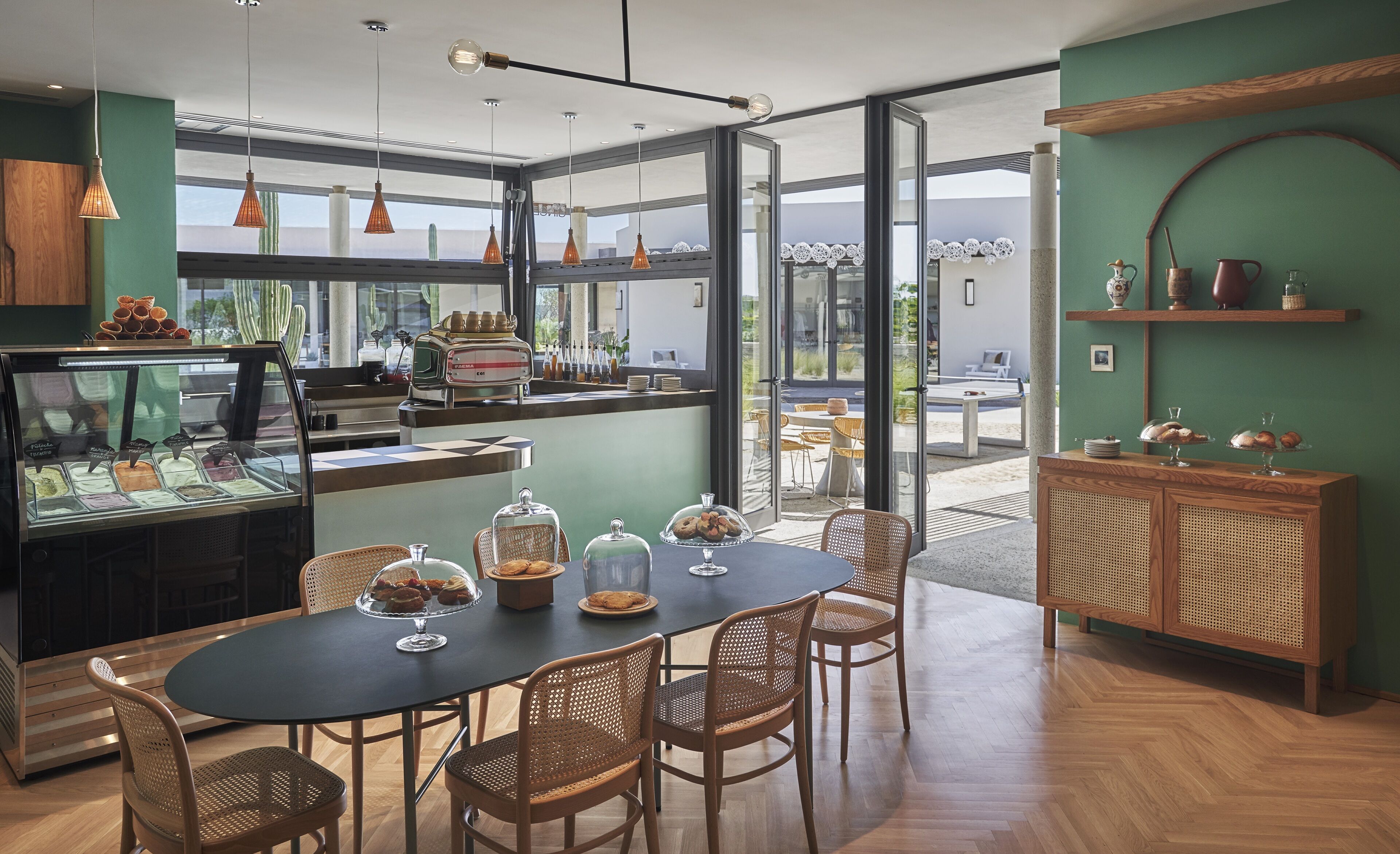 A café with a glass display case, wicker chairs, and a wooden counter with a coffee machine.