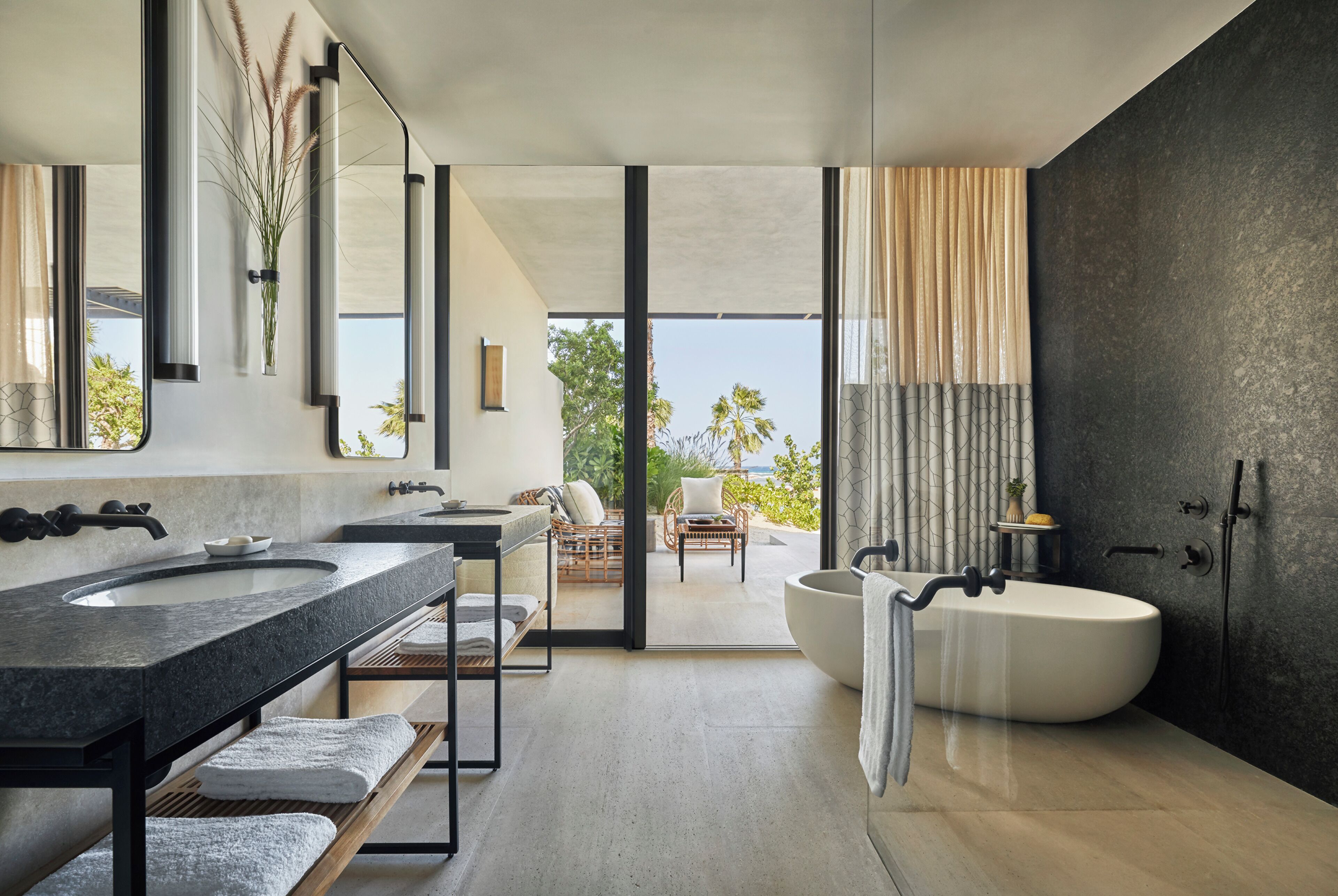 A modern bathroom with dual sinks, a freestanding bathtub, and a view of the outdoors.