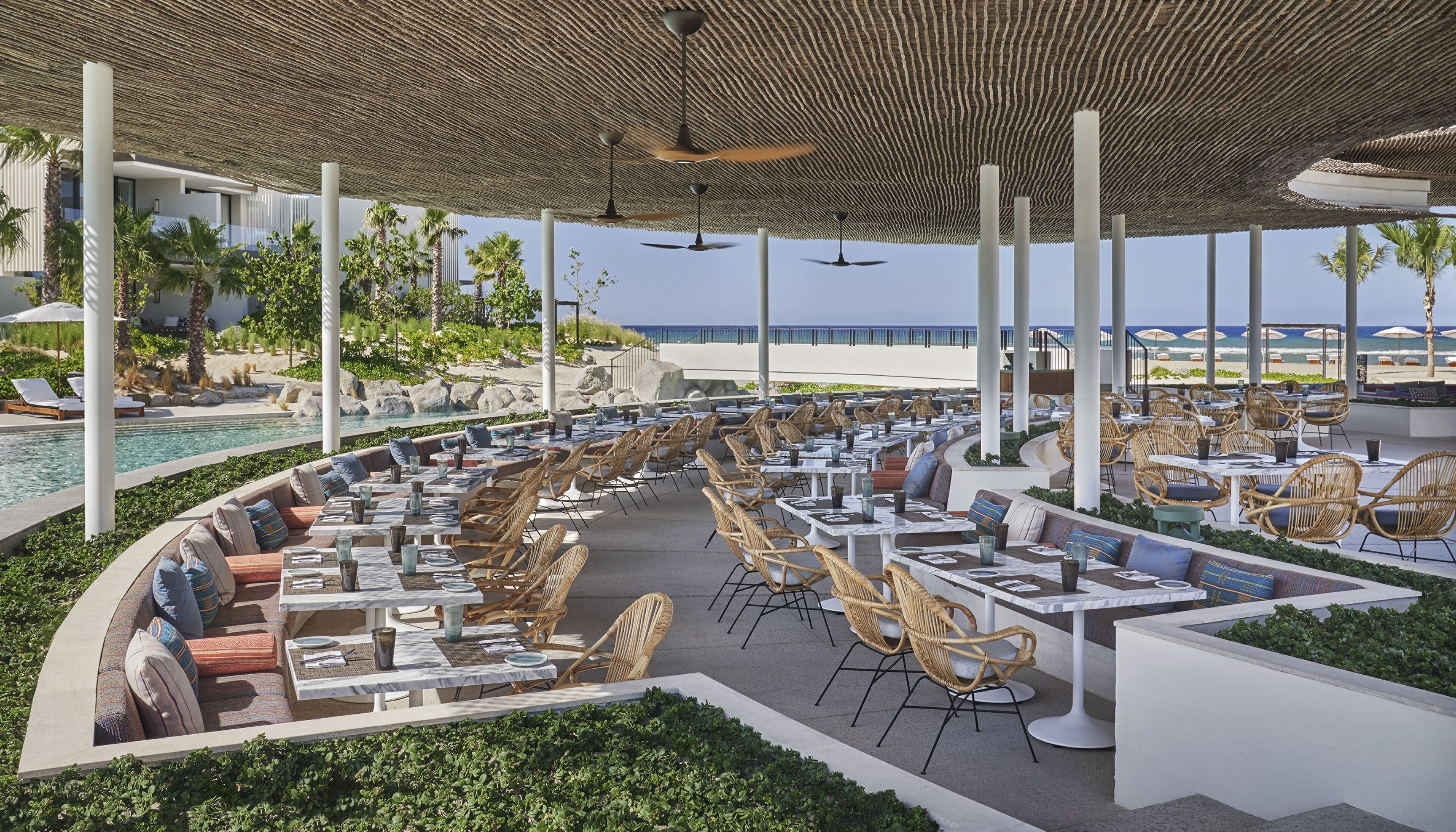 Un área de comedor al aire libre con mesas y sillas, una piscina y vistas al océano.