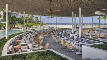 Un área de comedor al aire libre con mesas y sillas, una piscina y vistas al océano.