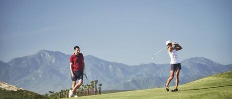 Two people playing golf on a course with mountains in the background.