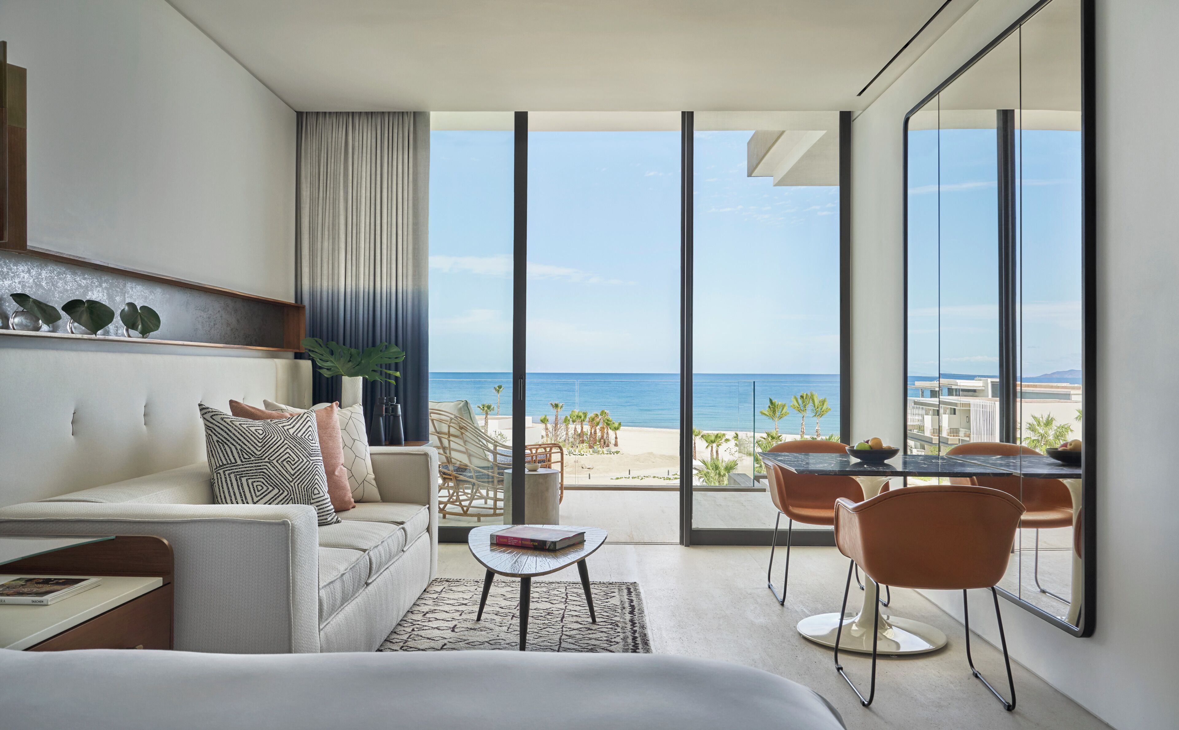 Habitación de hotel moderna con balcón grande, sofá, mesa de comedor y vistas al mar.