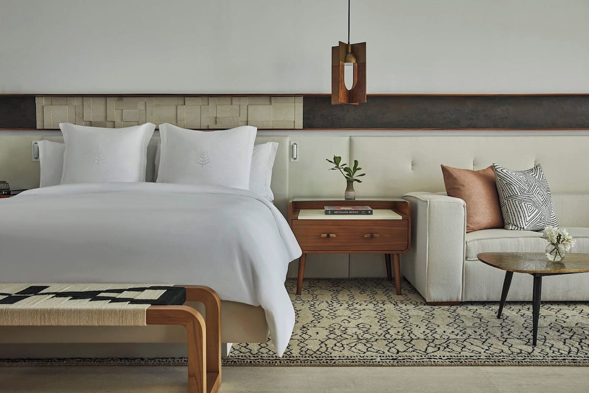 A modern hotel room with a large bed, a sofa, a coffee table, and a bedside table with a vase of flowers.