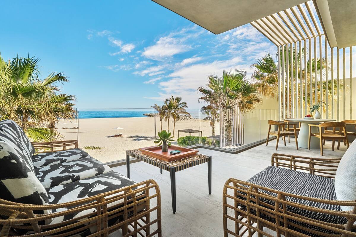 A beachside patio with wicker furniture, a table with a plant, and a view of the ocean.