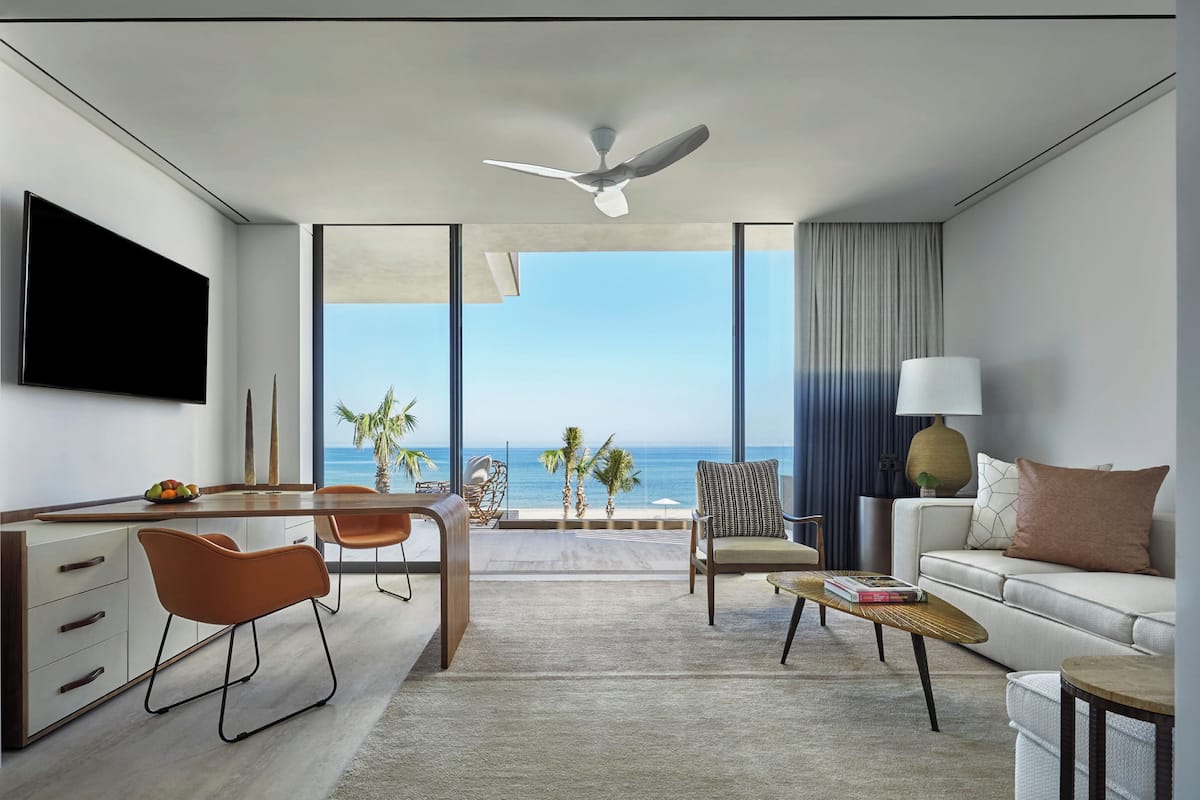A modern living room with a large TV, a dining area, and a sofa with a view of the ocean.