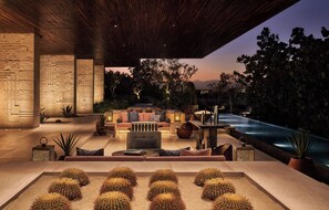 A modern outdoor lounge area with a stone wall, seating, and a pool. - Four Seasons Resort Los Cabos at Costa Palmas (La Ribera)