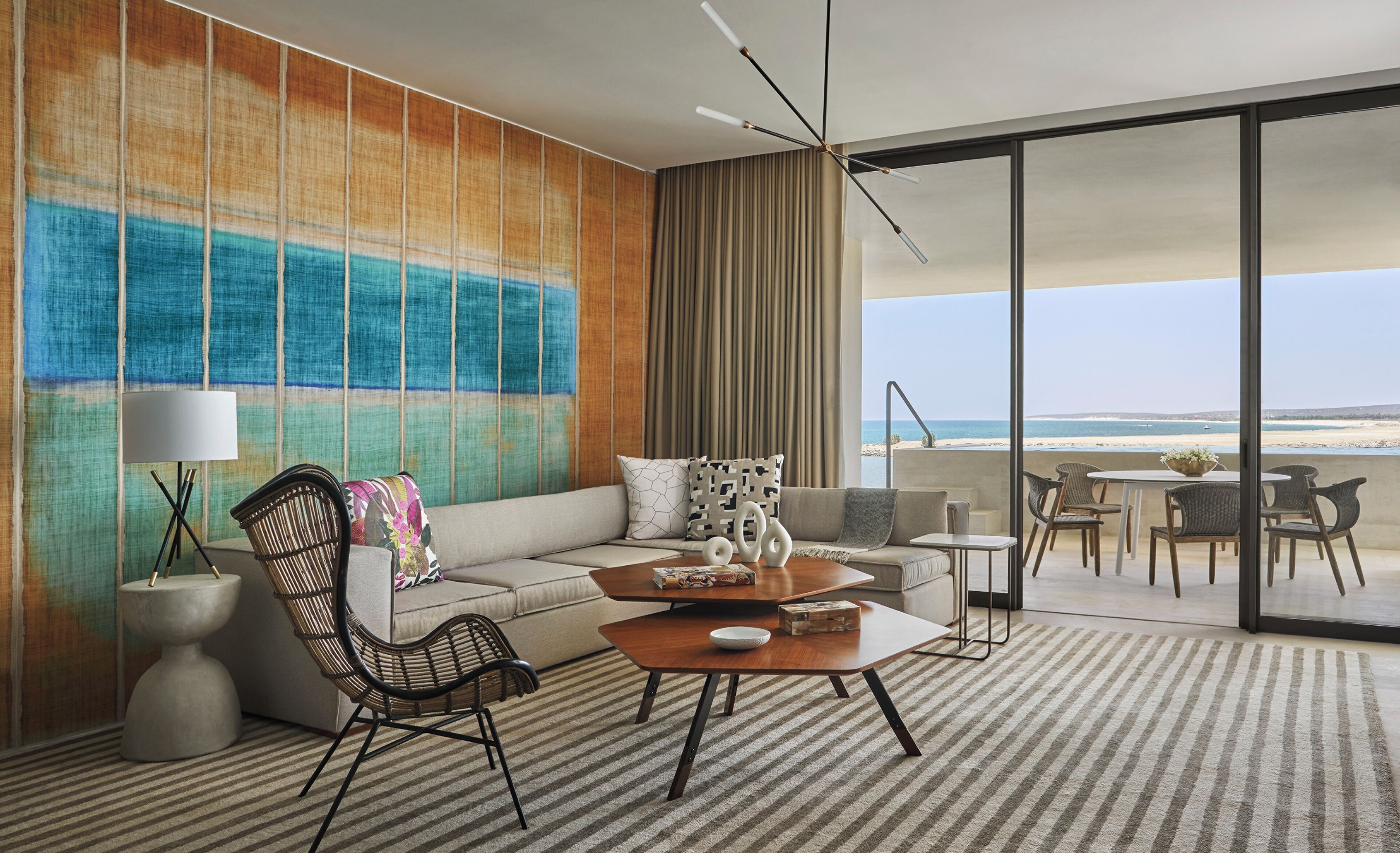 En moderne stue med et stort vindue der vender ud mod en strand, en sofa, et sofabord og et spiseområde med stole.