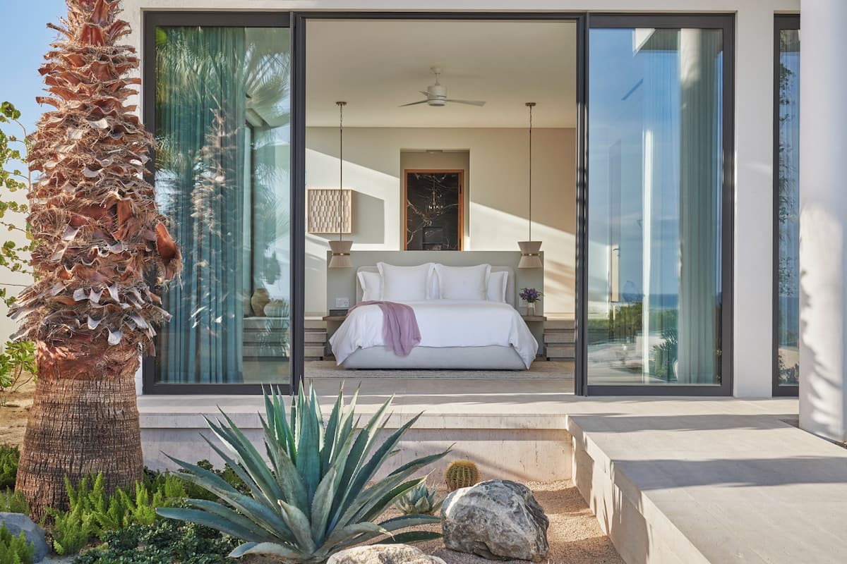 A modern bedroom with a large bed, a ceiling fan, and a view through glass doors.