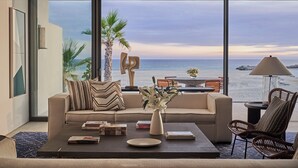 A modern living room with a large window overlooking the sea, a sofa, coffee table, and a chair.
