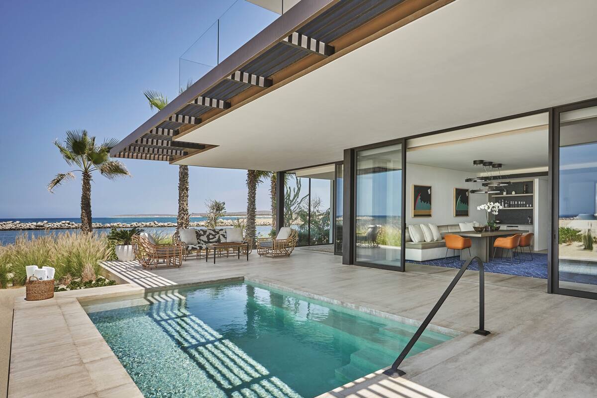 A modern outdoor pool area with a view of the ocean, furnished seating, and a glass-enclosed dining area.